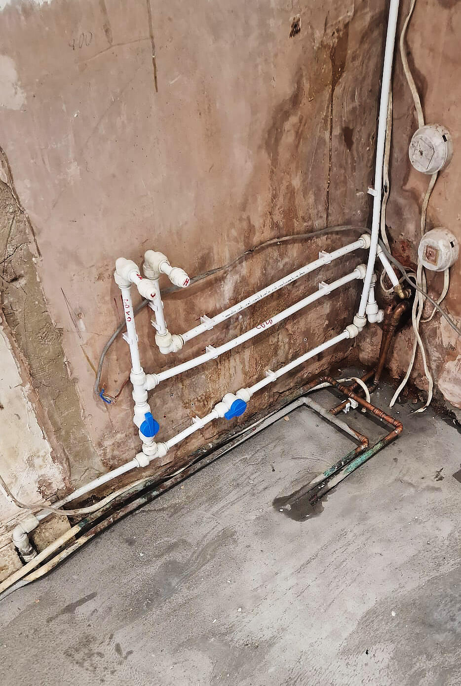 New first-fix plumbing pipework with labelled hot and cold isolation valves on a kitchen wall in Shepherds Bush