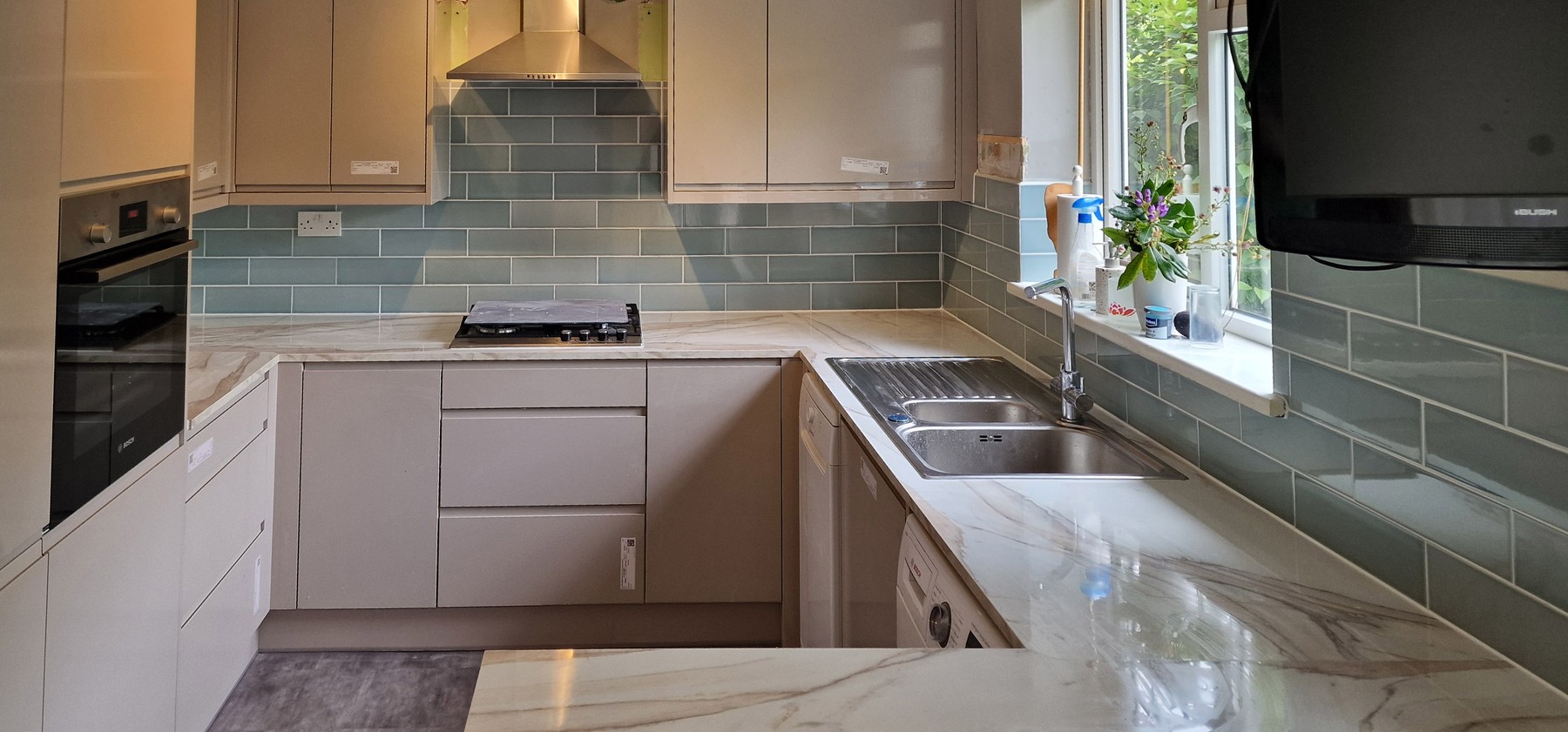 U-shaped fitted kitchen with marble-effect worktop and sage green metro tile splashback in Tooting, SW17