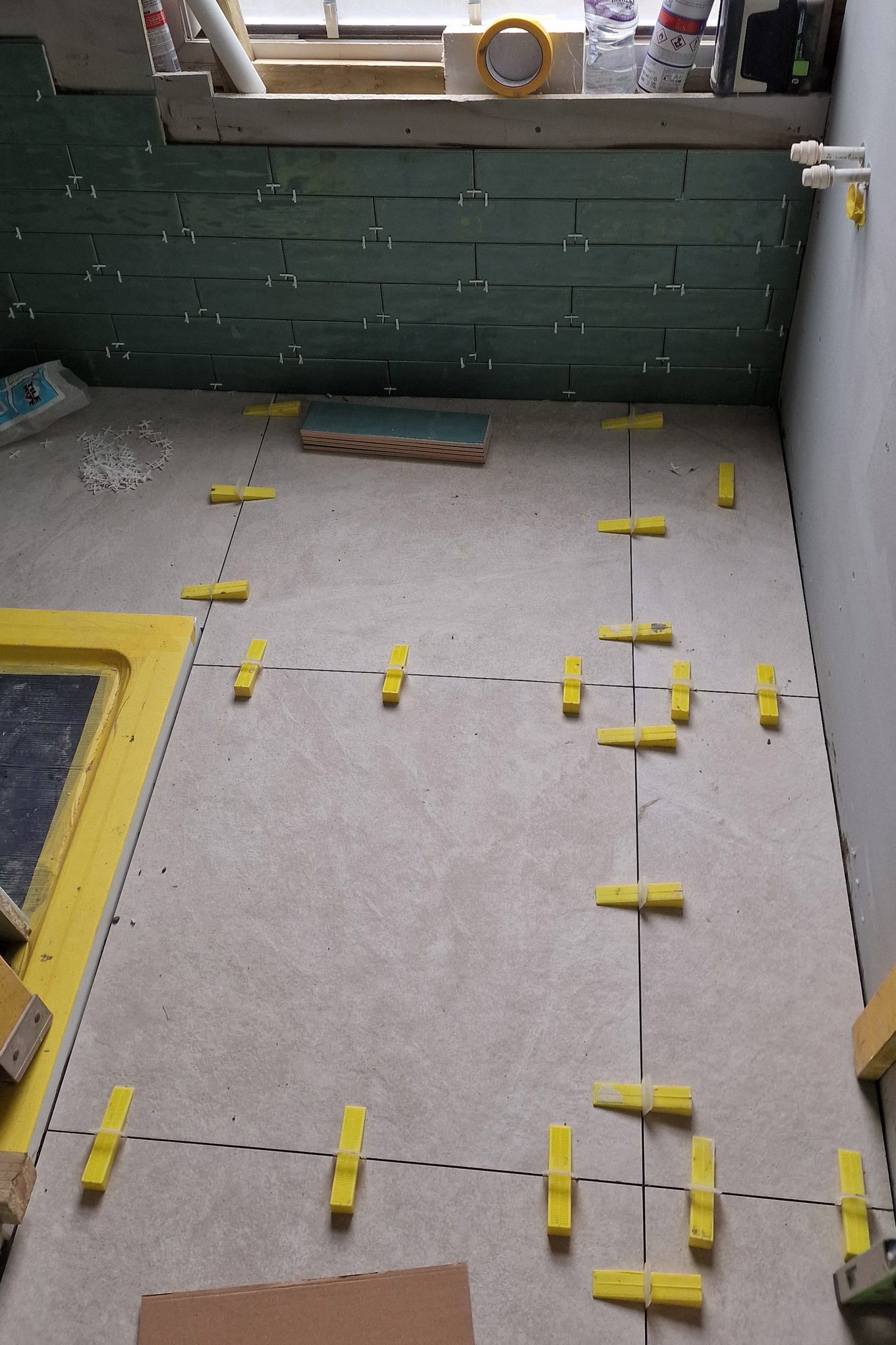 Large floor tiles being laid with levelling clips in a bathroom in Hampton Wick, green wall tiles behind