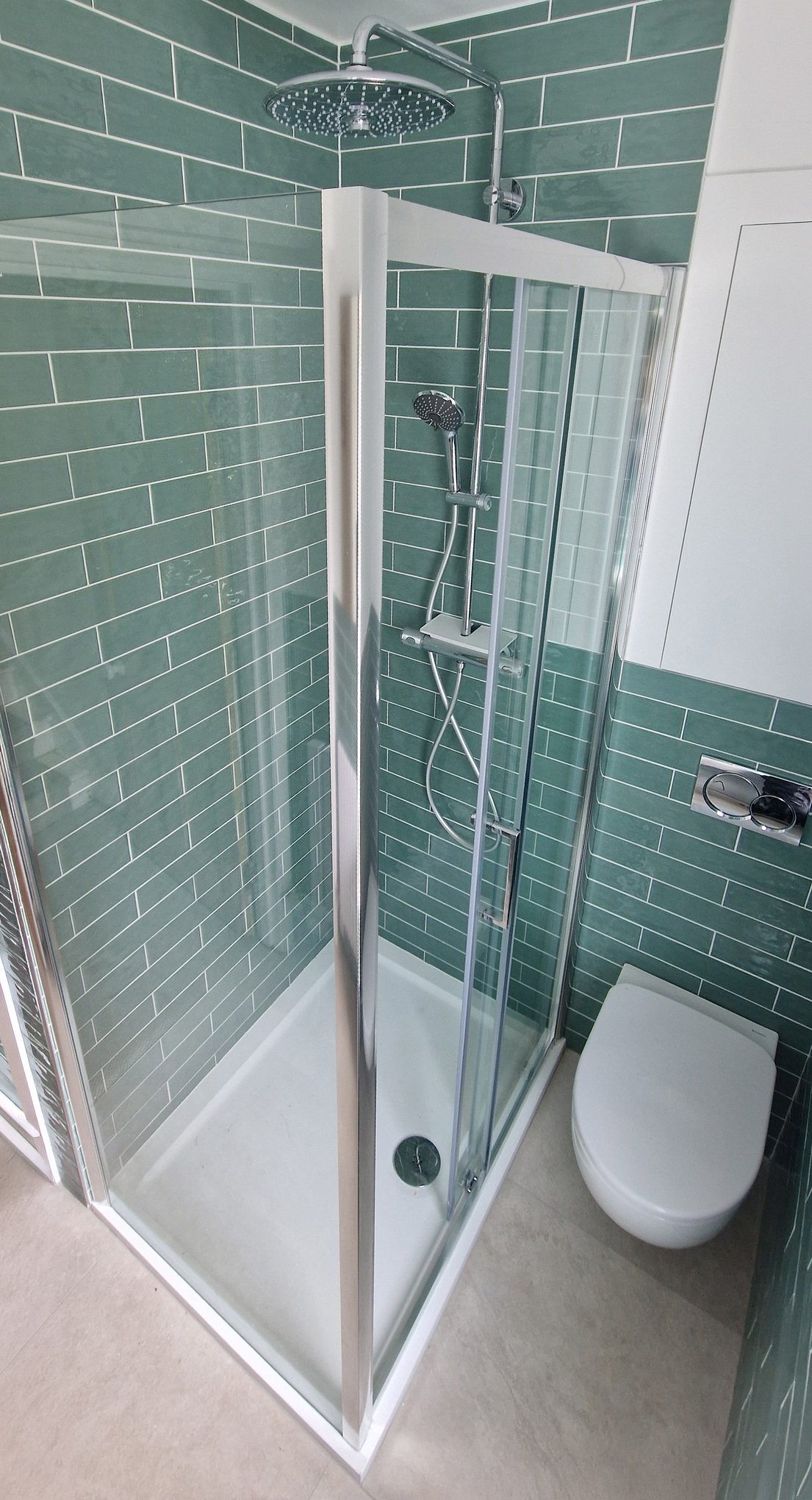 Bathroom in Hampton Wick with green tiles, a rain shower head, sliding glass door and wall-hung toilet