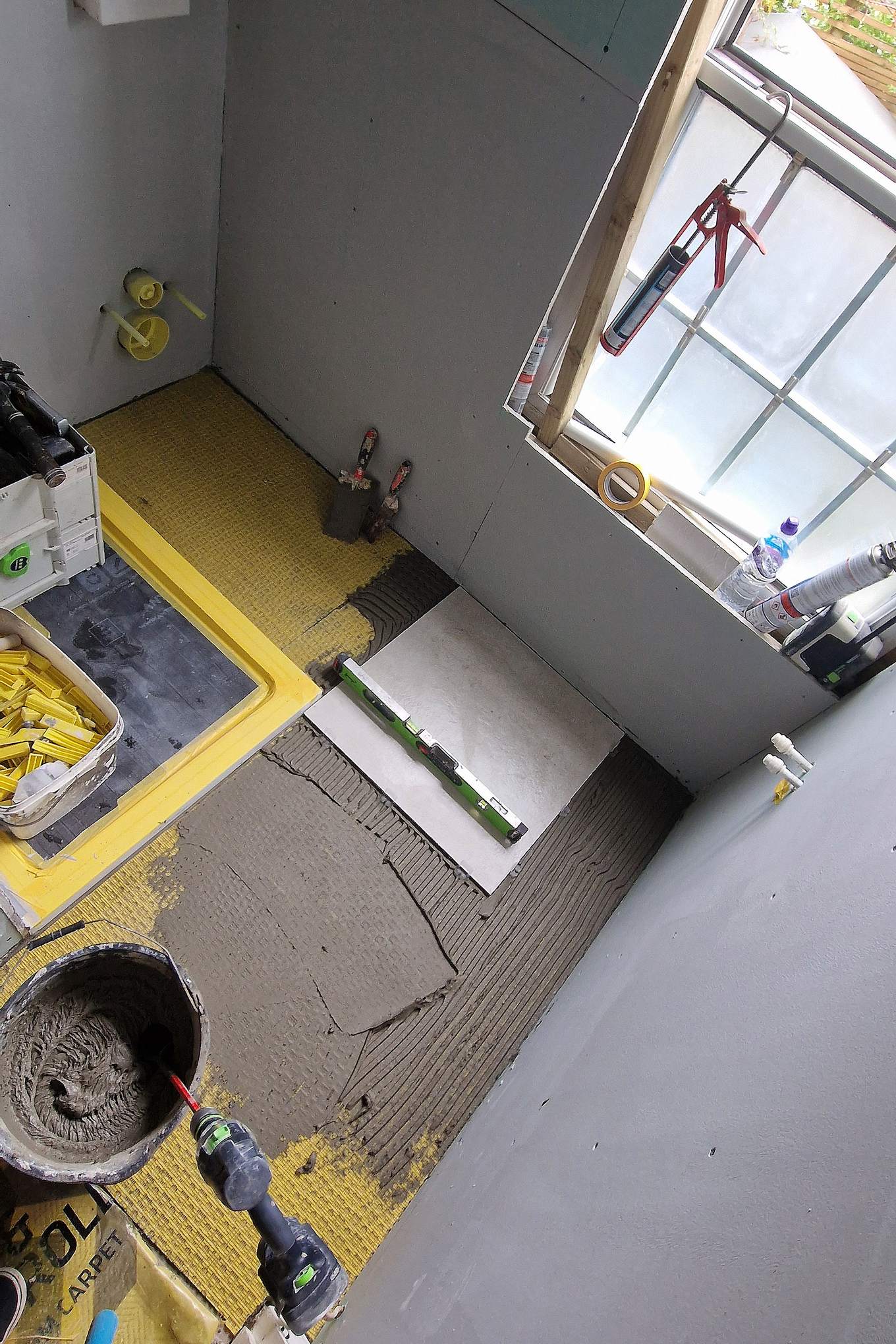 Bathroom in Hampton Wick before tiling: shower tray with a yellow waterproof membrane, wall boards and adhesive on the floor