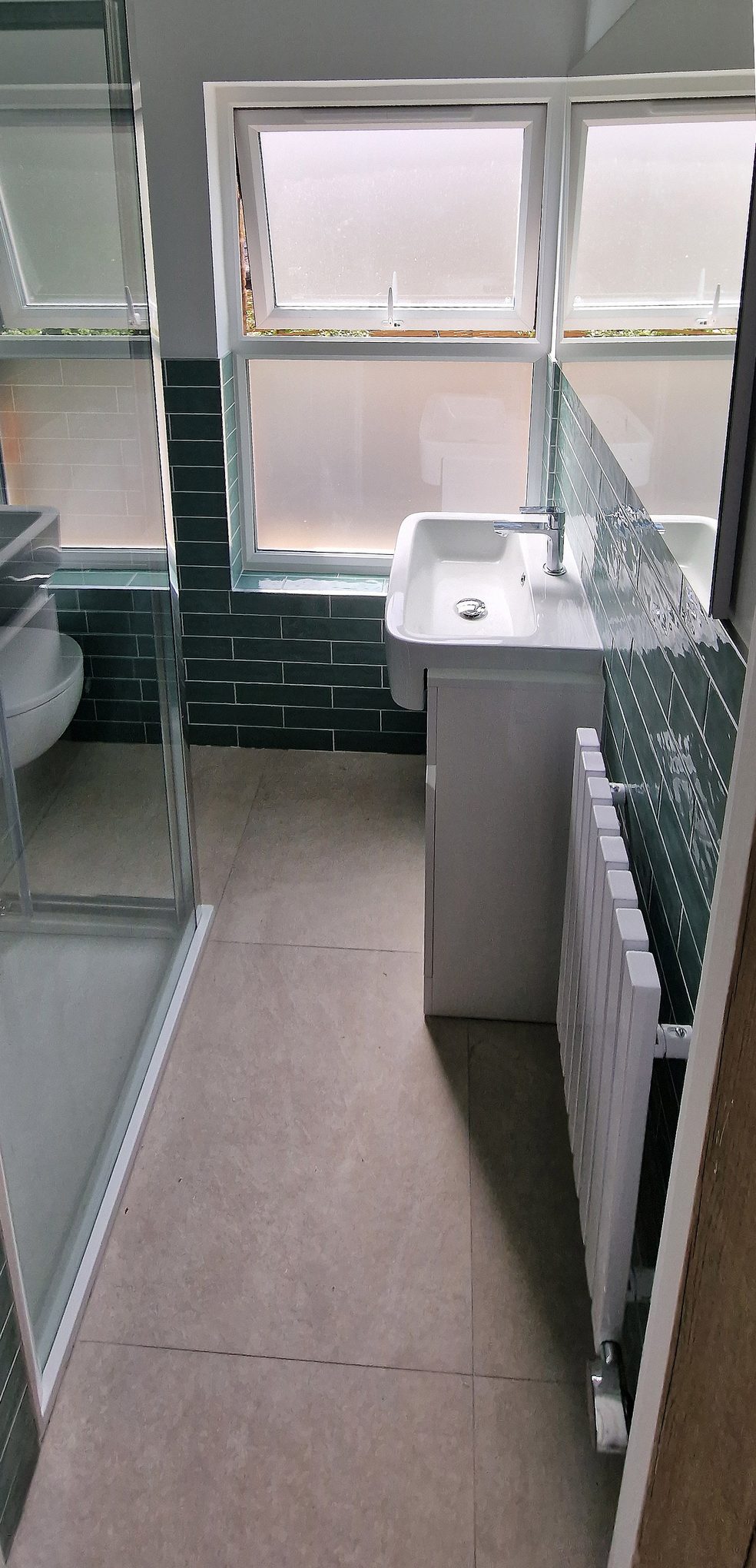 Bathroom vanity unit with basin, white radiator and large floor tiles below two frosted windows in Hampton Wick