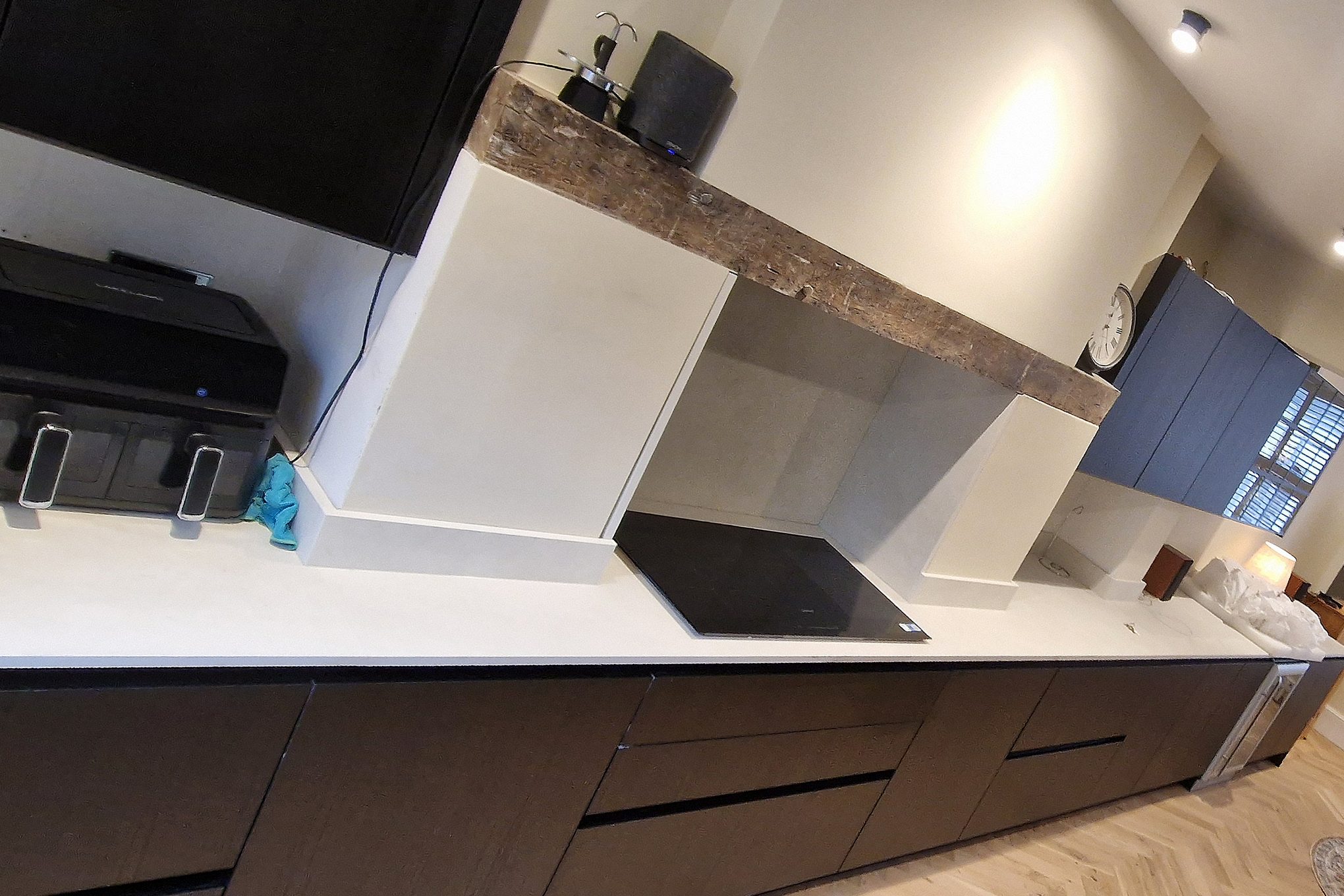 Fitted kitchen in Hampton Wick with dark units, white conglomerate worktop and a timber beam over the hob