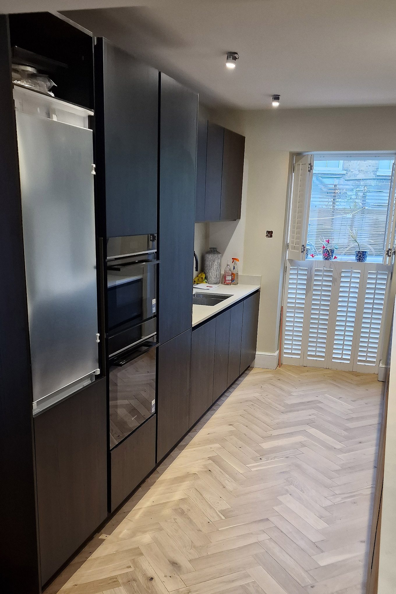 Tall kitchen units with two built-in ovens, one above the other, and a window with white shutters in Hampton Wick