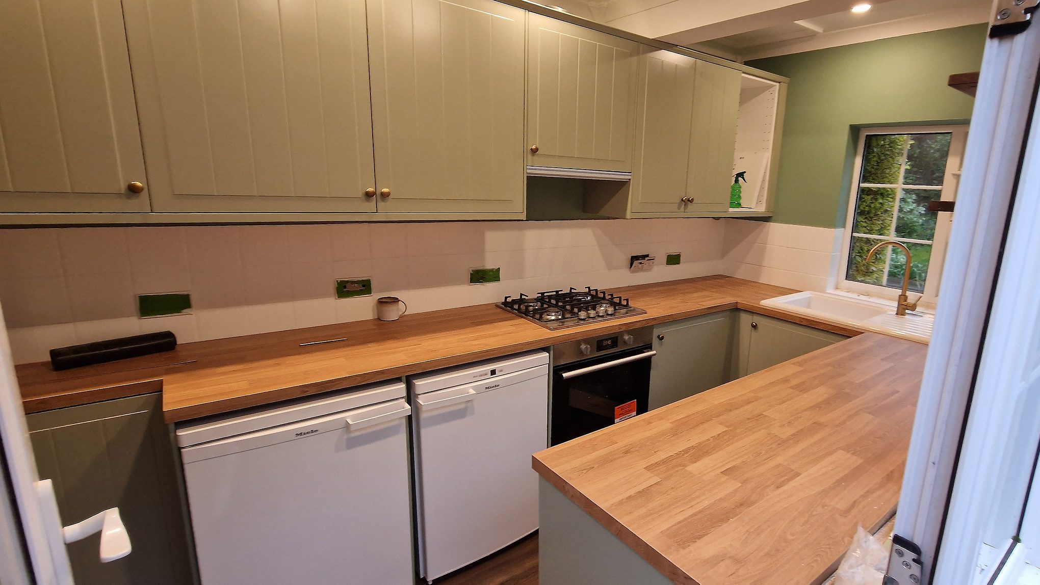 Sage green panelled kitchen units with an oak-effect laminate worktop in Worcester Park, Surrey
