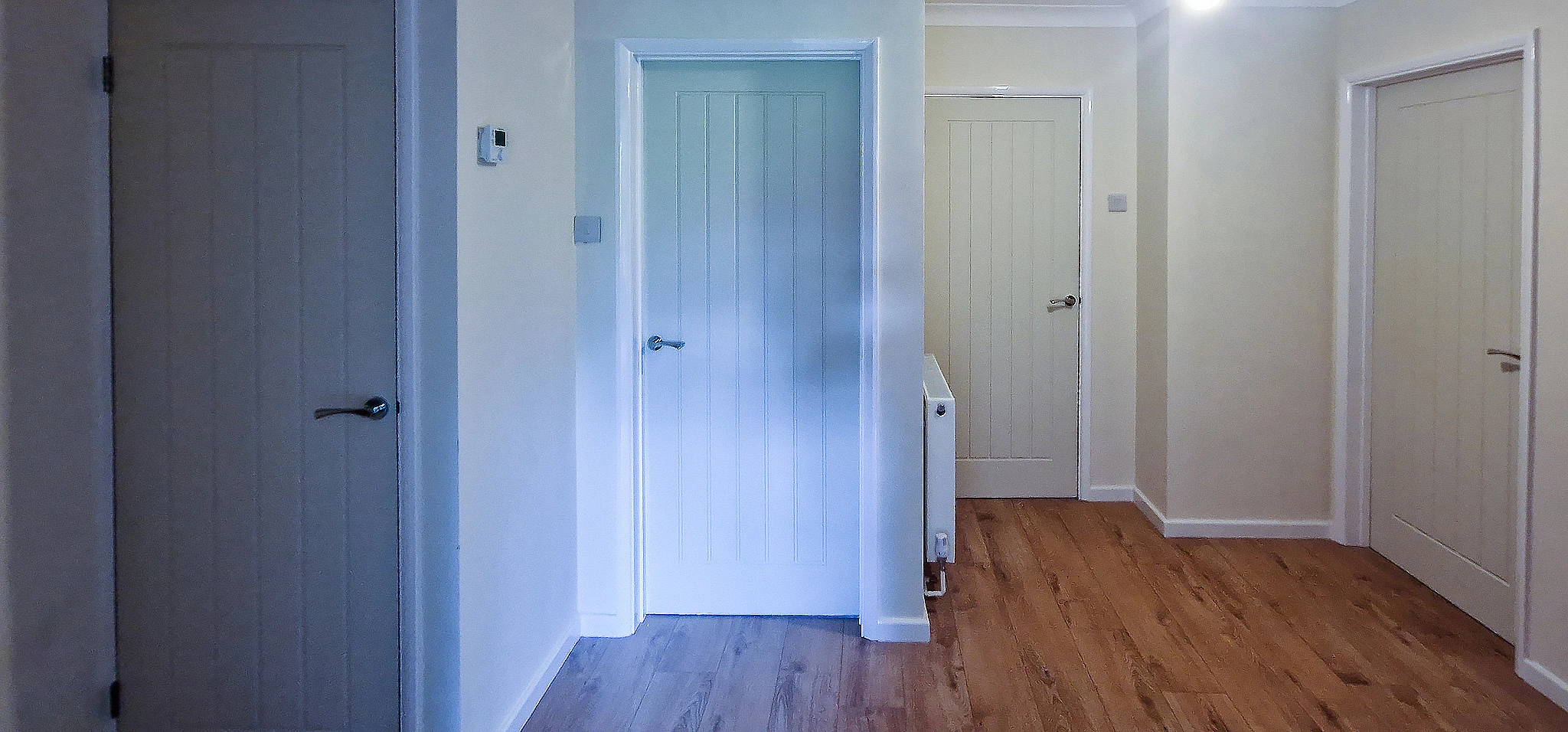 Howdens Dordogne internal doors fitted to existing frames in a Surrey hallway — seven-door project in one day Wide hallway view in Boxhill, Surrey showing Howdens Dordogne White Smooth Moulded doors fitted to existing frames with oak laminate flooring