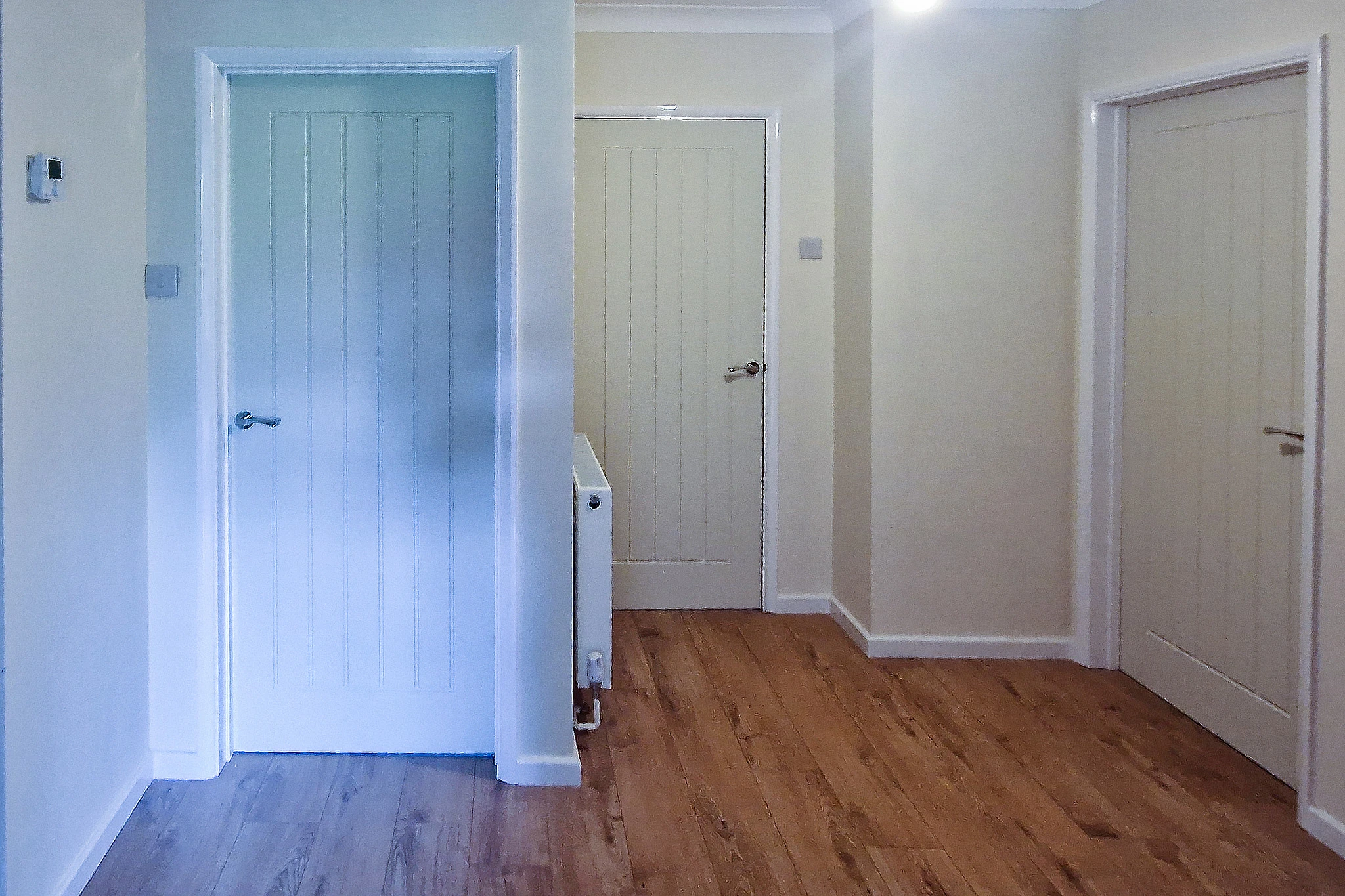 Internal door replacement in Boxhill, Surrey — moulded panel doors fitted to existing frames Three internal doors fitted in a hallway in Boxhill, Surrey — Howdens Dordogne moulded panel doors in white and sage with a radiator beneath