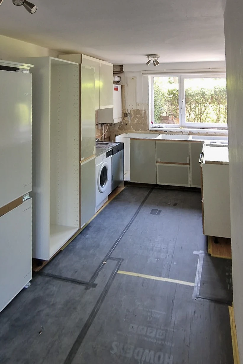 IKEA kitchen carcasses being installed in U-shape layout in Wandsworth, floor protected with hardboard during fitting