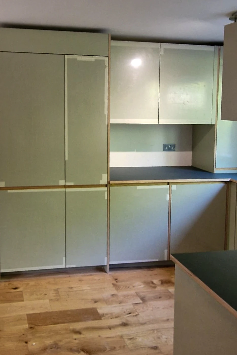 Tall and wall units with sage green Plykea fronts and dark laminate worktop in kitchen installation Wandsworth